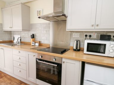 A kitchen with a sink stovetop oven kettle microwave and cabinets at Honeysuckle Cottage in Crossgates