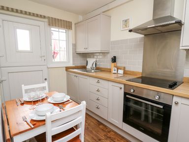 A kitchen with a wooden dining table set for four next to white cabinets and a stainless steel oven at Honeysuckle Cottage in Crossgates