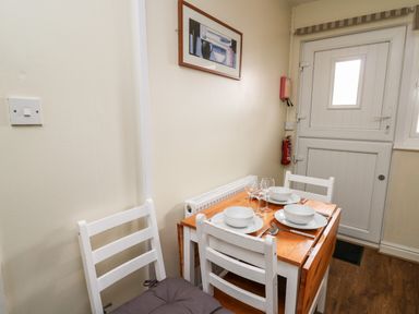 A dining area with a wooden table set with bowls glasses and cutlery and white chairs near a white door at Honeysuckle Cottage in Crossgates