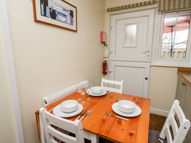 A small dining area with a wooden table set for three with white chairs and a white door and window in the background at Honeysuckle Cottage in Crossgates