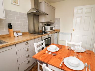 A kitchen with wooden dining table set for three with bowls wine glasses and cutlery at Honeysuckle Cottage in Crossgates