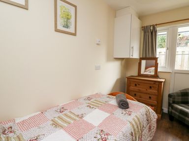 A bedroom with a single bed covered in a patchwork quilt a wooden chest of drawers with a mirror and a plaid armchair at Honeysuckle Cottage in Crossgates