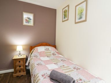 A single bed with a patchwork quilt and folded towel next to a wooden nightstand with a lamp and framed pictures on the walls at Honeysuckle Cottage in Crossgates