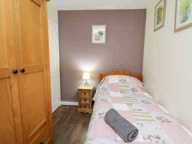 A bedroom with a single bed, bedside table with lamp, wooden wardrobe, and framed pictures on the walls at Honeysuckle Cottage in Crossgates