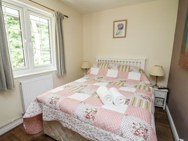A bedroom with a bed covered with a patchwork quilt and two rolled towels on top at Honeysuckle Cottage in Crossgates