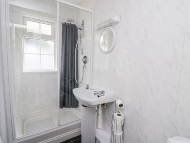 A bathroom with a shower enclosure sink mirror and toilet paper holder at Honeysuckle Cottage in Crossgates