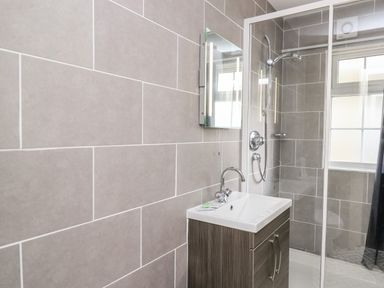 A bathroom with a sink and wooden cabinet next to a tiled shower at Honeysuckle Cottage in Crossgates