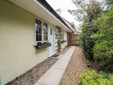 A walkway along a house exterior with flower boxes on windows and a wooden gate at Primrose Cottage in Crossgates