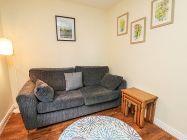 A living room with a grey sofa three framed pictures on the wall a floor lamp round rug and nesting tables at Primrose Cottage in Crossgates