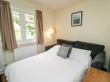 A bedroom with a sofa bed white bedding cushions lamp and a window with curtains at Primrose Cottage in Crossgates