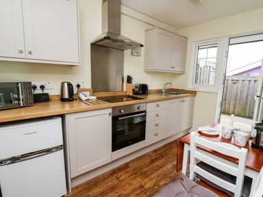 A kitchen with white cabinets wooden countertops a stove oven microwave kettle toaster and a small dining table with chairs at Primrose Cottage in Crossgates