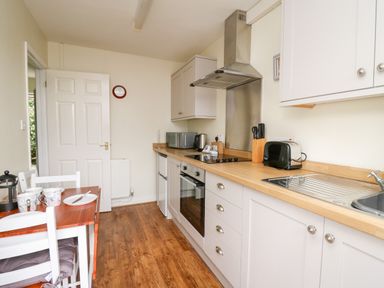 A kitchen with a dining table set with cups and plates beside cabinets with appliances at Primrose Cottage in Crossgates