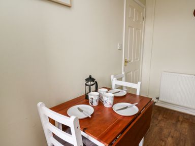 A small wooden dining table with two white chairs cups plates and knives in a room at Primrose Cottage in Crossgates