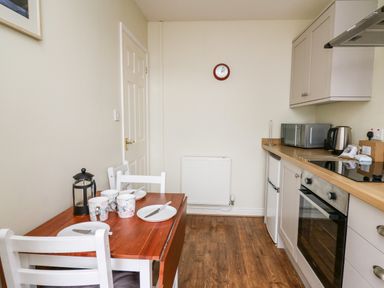 A kitchen with a wooden table and white chairs a microwave kettle oven and fridge at Primrose Cottage in Crossgates