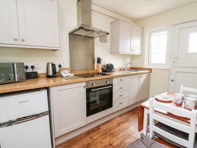 A kitchen with wooden countertop white cabinets oven microwave kettle toaster and a small dining table at Primrose Cottage in Crossgates