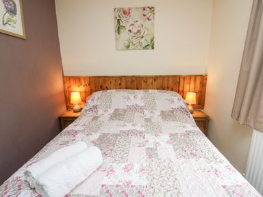 A bedroom with a double bed with floral quilt and two bedside tables with lamps at Primrose Cottage in Crossgates