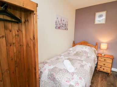 A bedroom with a single bed with floral quilt a wooden nightstand with a lamp and wooden wardrobe at Primrose Cottage in Crossgates