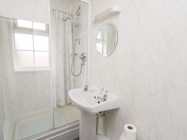 A bathroom with a shower enclosure a sink a round mirror and a roll of toilet paper at Primrose Cottage in Crossgates