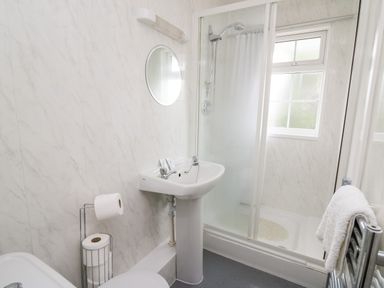 A bathroom with a shower cubicle sink round mirror and towel rail at Primrose Cottage in Crossgates