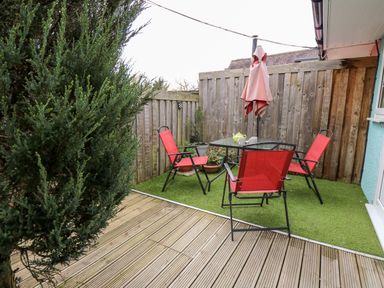 An outdoor patio with red chairs a glass table and a pink umbrella at Primrose Cottage in Crossgates