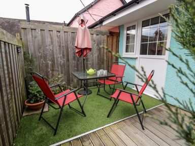 An outdoor patio area with red chairs a glass table a closed umbrella and potted plants at Primrose Cottage in Crossgates