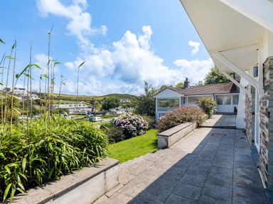 An outdoor patio area with stone tiles and steps leading to a grassy garden with bushes and flowers at Beach Haven in Polzeath