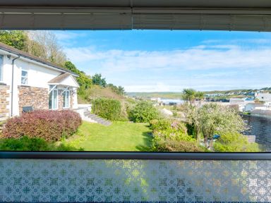 View of a garden with bushes and trees along with houses and hills in the distance at Beach Haven in Polzeath