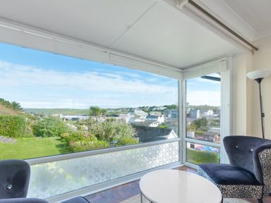 A corner lounge area with two chairs a round table and floor lamp overlooking a garden and residential area at Beach Haven in Polzeath