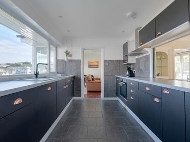 A galley kitchen with black cabinets and a window overlooking buildings at Beach Haven in Polzeath