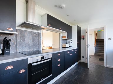 A kitchen with black cabinets a stainless steel oven countertop appliances and an open door showing a staircase at Beach Haven in Polzeath