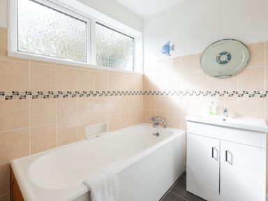 A bathroom with a bathtub towel on the side a white sink with cabinet and a wall mirror at Beach Haven in Polzeath