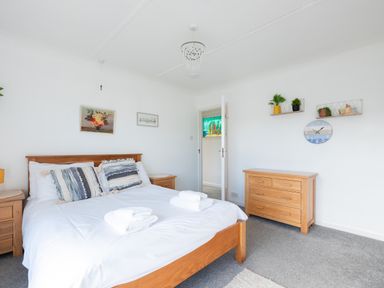 A bedroom with a wooden bed and white bedding next to wooden nightstands and a wooden dresser with plants on shelves at Beach Haven in Polzeath
