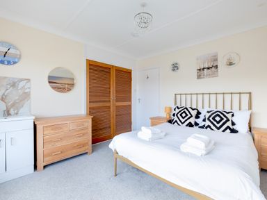 A bedroom with a double bed with patterned pillows and folded towels a wooden dresser a sink and wooden closet doors at Beach Haven in Polzeath