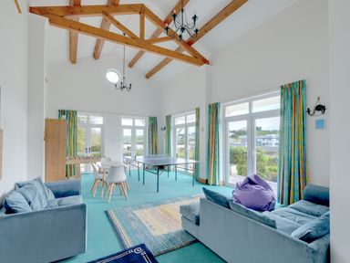 A room with blue sofas a table tennis table a foosball table white chairs and colorful curtains at Beach Haven in Polzeath