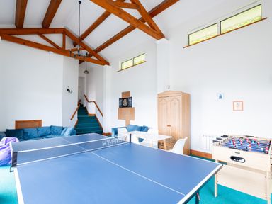 A game room with a ping pong table foosball table couches and a wooden cabinet at Beach Haven in Polzeath