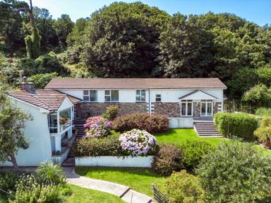 A house with a garden and flowers surrounded by trees at Beach Haven in Polzeath