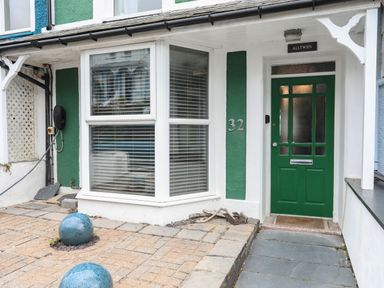 The exterior of a house with a green door and large bay window with white blinds and decorative blue spheres on the paved front yard at Alltwen in Borth-y-Gest