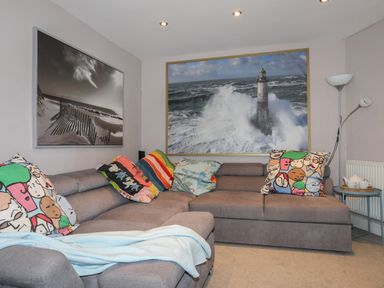 A living room with a gray sectional sofa with colorful cushions and two framed pictures on the walls at Alltwen in Borth-y-Gest