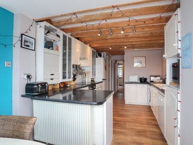 A kitchen with white cabinets black countertops wooden beams and string lights at Alltwen in Borth-y-Gest