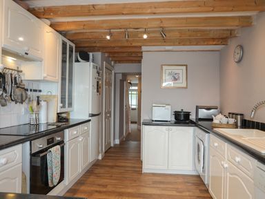 A kitchen with wooden beams on the ceiling white cabinets black countertops and various appliances at Alltwen in Borth-y-Gest