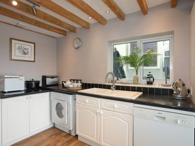 A kitchen with white cabinets black countertop washing machine dishwasher and a window with a plant at Alltwen in Borth-y-Gest