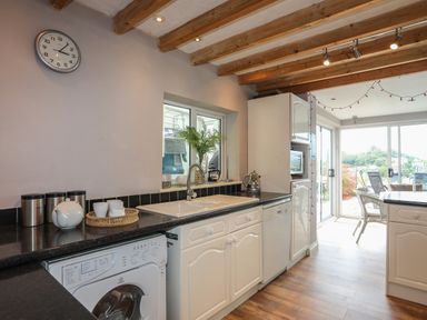 A kitchen with a sink washing machine dishwasher and sliding glass doors leading to an outdoor area at Alltwen in Borth-y-Gest