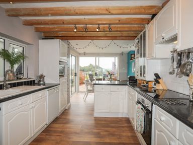 A kitchen with white cabinets black countertops wooden beams on ceiling and a dining area with glass doors at Alltwen in Borth-y-Gest