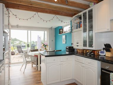 A kitchen with white cabinets and black countertops next to a dining area with wicker chairs and a table at Alltwen in Borth-y-Gest