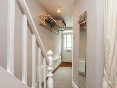 A hallway with a white banister on the left a wall-mounted storage rack and a mirror on the right near the front door at Alltwen in Borth-y-Gest