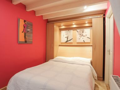 A bedroom with a double bed white bedding wood wardrobe with floral paintings on a red wall at Alltwen in Borth-y-Gest