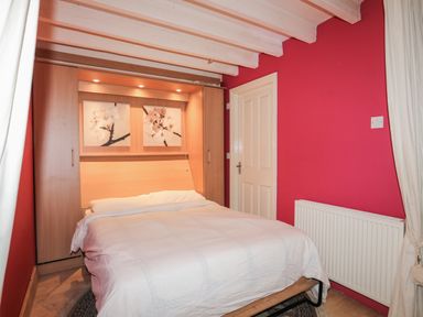 A bedroom with a bed white bedding wood storage units and floral pictures on a wall at Alltwen in Borth-y-Gest