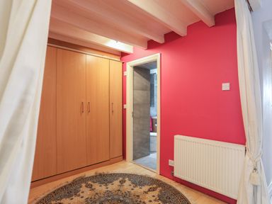 A room with a wooden wardrobe a round carpet a red wall a white radiator and a doorway leading to a bathroom at Alltwen in Borth-y-Gest