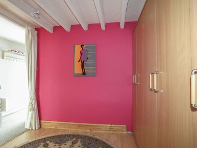 A room with pink walls a wall painting a wooden wardrobe a round rug and white curtains at Alltwen in Borth-y-Gest