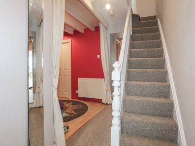 A hallway with carpeted stairs on the right and a red wall with a door and a radiator on the left at Alltwen in Borth-y-Gest